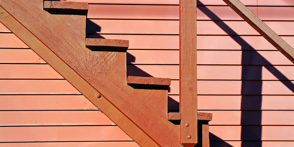 Person measuring and marking stair stringer cuts on wooden board with calculator and triangle square tools