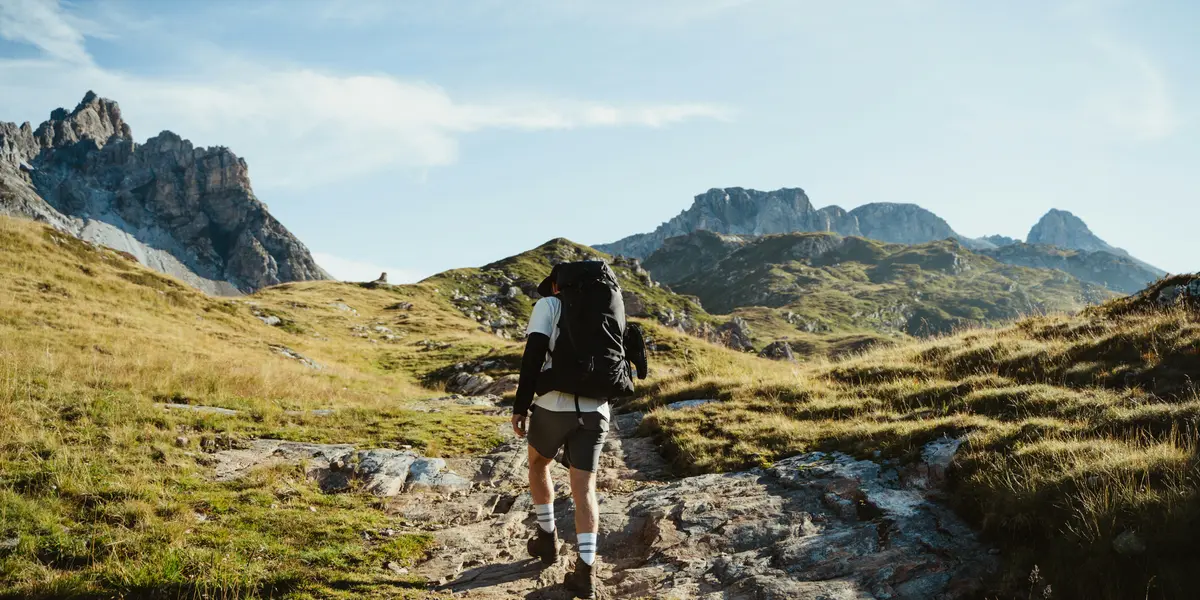 Hiker using compass and triangulation methods to navigate through wilderness terrain with mountains in background